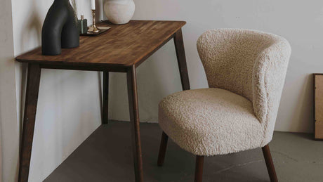 A simple white boucle dining chair with wooden legs next to a simple wooden table